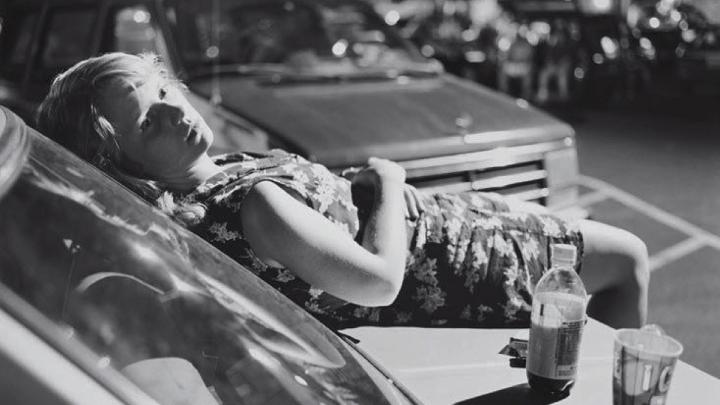 black and white photo of young woman laying on the hood of a car