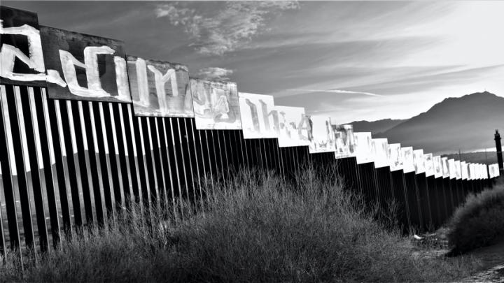 A photograph of the border wall stretching toward a mountain in the distance