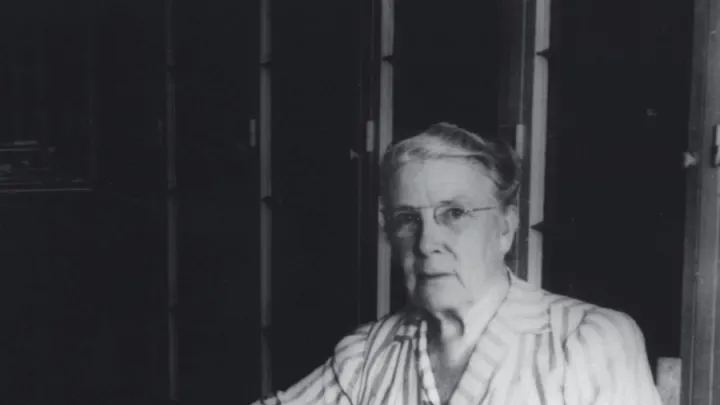 Photograph of a stout middle-aged woman seated at her desk, writing