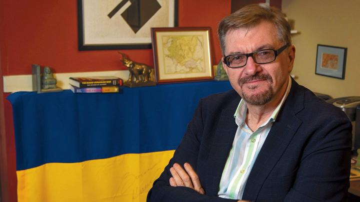 Serhii Plokhy in his Harvard office, smiling with his arms crossed. Behind him hangs a Ukrainian flag signed by Kyiv mayor Vitali Klitschko