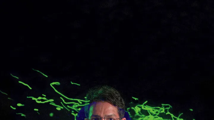 Vamsi Mootha with an image from his lab showing thread-like mitochondria (green) moving within a cell.