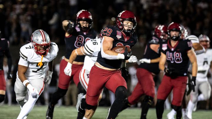 Harvard Football player 29 runs with football with Brown players running after along with other Harvard players