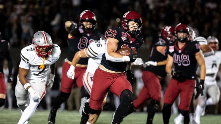 Harvard Football player 29 runs with football with Brown players running after along with other Harvard players