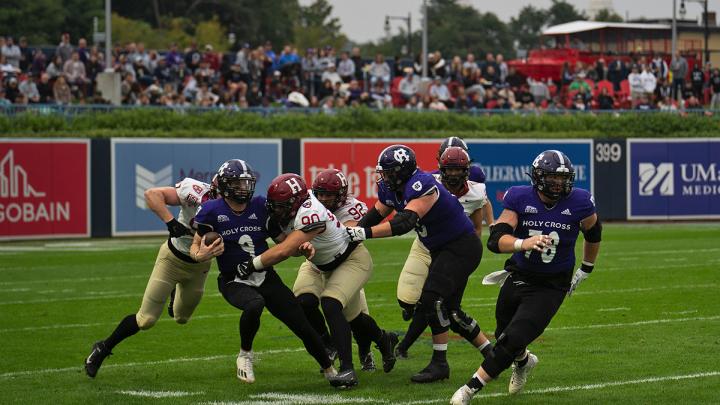 Holy Cross player has ball and Harvard players try to tackle with additional Holy Cross players in pursuit