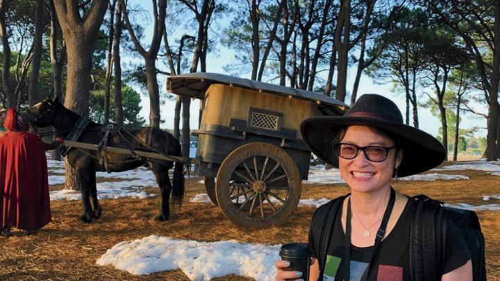 A woman with a backpack and a cup of coffee in a forest with fake snow and a small horse-drawn wagon. 