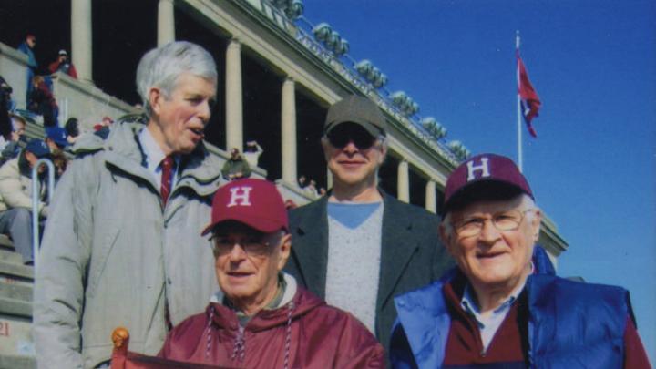 Alumnus Paul Lee ’46 carries the (replica) Little Red Flag at the 2012 Harvard-Yale game. Steve Goodhue ’51 is beside him; Spencer Ervin ’54 and Jeff Lee ’74 stand behind.