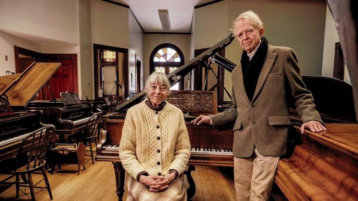 An older couple standing in a large room filled with pianos