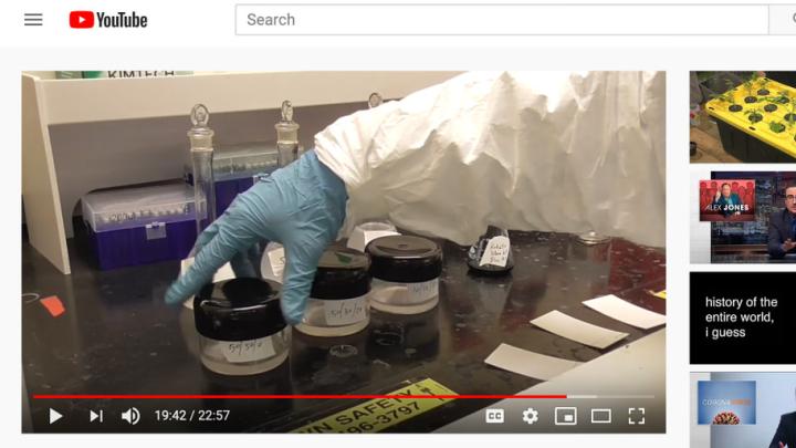 A human arm wearing a white goat and rubber glove in a lab setting handles three containers of lab chemicals