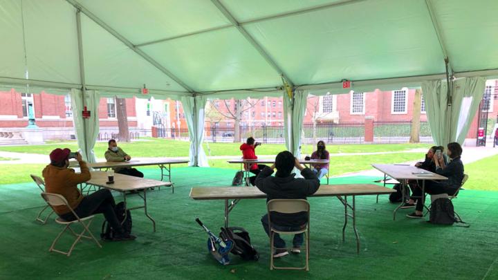 Students gather in desks under a tent, a pilot of outdoor instruction for performance-based courses
