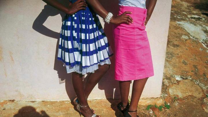 The lower halves of two women stylishly dressed in bright colored skirts and high heels