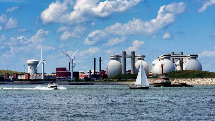 view from water of island holding giant steel eggs and wind turbines of wastewater treatment plant