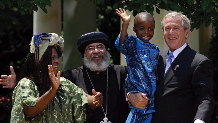 George W. Bush, speaking about PEPFAR (the global AIDS initiative) and holding Baron Mosima Loyiso Tantoh, with Kunene Tantoh, the boy’s mother, then suffering from AIDS, and Bishop Paul Yowakim, May 30, 2007, the White House