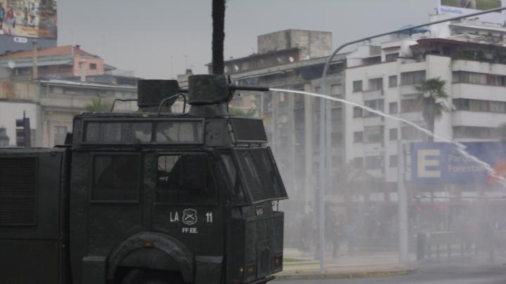 Stray dogs chase police trucks blasting water to break up a student protest in Santiago.