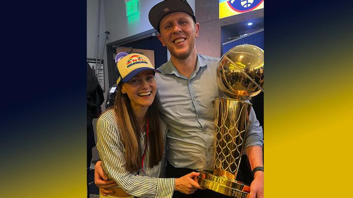 Balcetis smiling and holding the NBA championship trophy, with his arm around his wife
