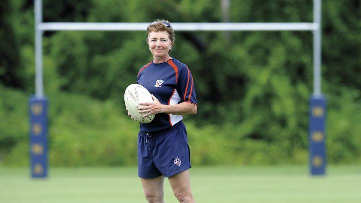 Holding a rugby ball, Sue Parker stands before rugby goalposts. She is Harvard&rsquo;s first varsity coach in the sport. 