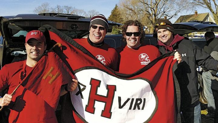 Members of the undefeated 2001 Crimson football team show flags at a 2011 tailgate in New Haven. Jared Lewis &rsquo;02, far left, holds the ancient Little Red Flag, which has been to many Harvard-Yale football games. He designed the new flag, and Kelly Goff made it. It is brandished, from left, by Justin Stark &rsquo;02, Jason Hove &rsquo;02, and Samuel Taylor &rsquo;02.
