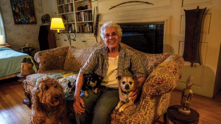 Elizabeth Thomas shown on her couch at home with her own small dogs, Chapek and Kafka, and her son’s large dog, Clover, whom she watches when he is away.