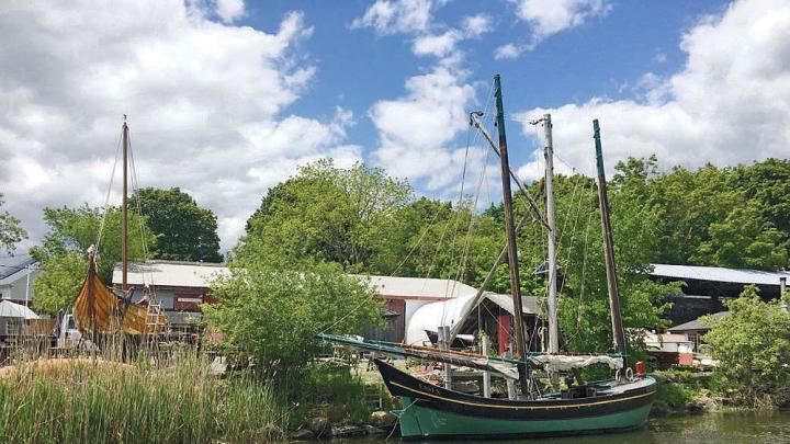 A boat, sails furled, docked near the Essex Historical Society and Shipbuilding Museum. 