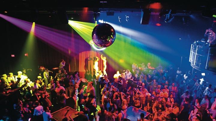 A disco ball and DJ overlook the <i>Donkey Show</i> audience as cast members enact a scene.