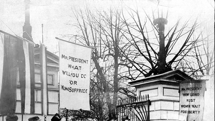 President Wilson passes “Silent Sentinels” as he leaves the White House grounds.