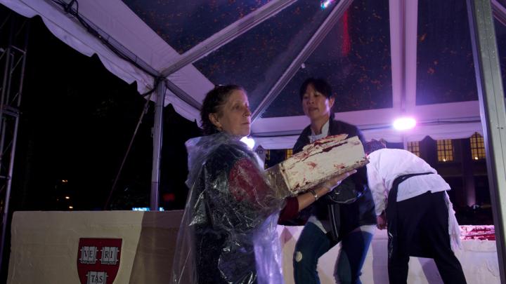 The moment the crowd has been waiting for: Joanne Chang ’91 begins to remove layered sheets from her massive red velvet cake so pieces can be cut and served.