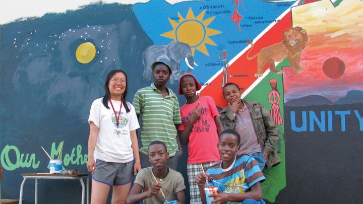 Xue standing in front of the mural that she and her students painted together, an elaborate map of Namibia