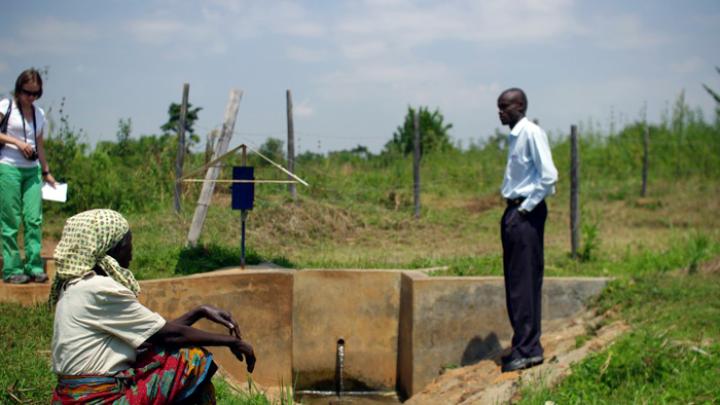 At a water collection site near Busia, Kenya, Leonard Bukeke, rural water project coordinator for IPA, shows the author around and introduces her to Seline Luyemba (foreground), the local resident who is responsible for making sure the dispenser gets refilled when it's near empty.