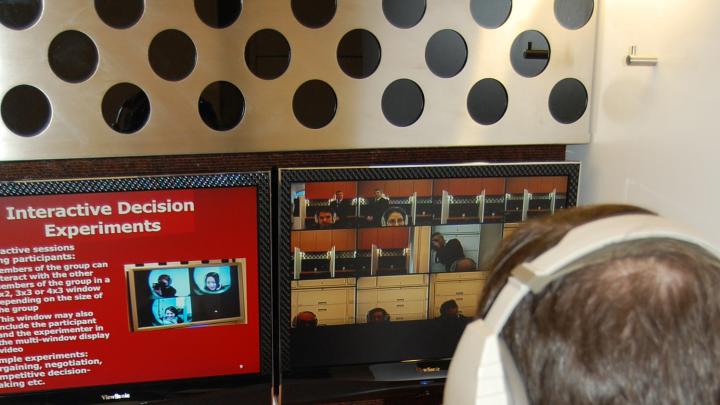 Each cubicle has two monitors that allow study participants to see the other participants (on the right-hand screen) alongside information or a stimulus presented by the experiment leader. Participants can communicate with one another through their headphones.