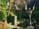 Bronze sculpture of a winged face and torso stands in a lush green garden