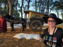 A woman with a backpack and a cup of coffee in a forest with fake snow and a small horse-drawn wagon. 