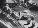 black and white photo of young woman laying on the hood of a car