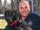 Harvard police officer Steven Fumicello poses with black Labrador retriever Sasha. 