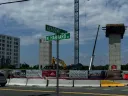 Construction site at the intersection of Academic Way and North Harvard Street. Two tall, unfinished concrete structures stand behind a fenced area with various signs and banners.
