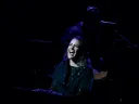 Madeline Benson singing at the piano, her face lit up on an otherwise dark stage