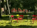 Colorful metal chairs arranged in a circle on the grass under trees in Harvard Yard. Red brick buildings in the background.