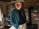 Tom Lee standing in his home in New Hampshire, surrounded by books and a brick fireplace.