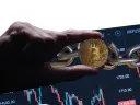 Cryptocurrencies are forms of digital assets stored on blockchains; image depicts hand holding representation of bitcoin over chain
