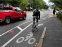 A cyclist rides in a bike lane that ends abruptly near a sidewalk as a red pickup truck passes nearby.