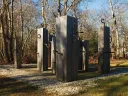 Wooden pillars with curved metal hooks arranged in an outdoor installation.