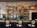 Elegant bar with glass shelves stocked with liquor bottles, three cane-back chairs, and hanging pendant lights.