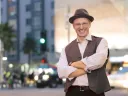 Salvador Litvak smiles, arms crossed, in a vest and hat on a city street.