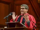 Rakesh Khurana, wearing a red doctoral robe, speaking at a podium 