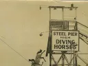 A woman and a horse jump off a large platform into water