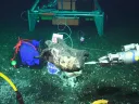 A robotic arm interacting with an underwater object on the ocean floor.