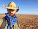 Javier Ortega-Hernández wearing a straw hat and blue scarf stands in a vast, arid landscape.
