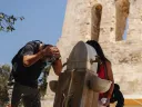 Man splashing water on his face at outdoor fountain beside woman holding cup near stone building.
