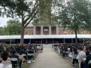 Outdoor convocation ceremony with a crowd seated under a tent, against Memorial Church