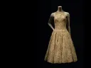 A vintage golden dress with a fitted bodice and flared skirt displayed on a mannequin.