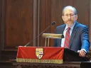 Alan Garber speaking at a podium in Memorial Church, with wooden panels in the background.