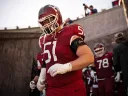Harvard football player in red jersey 51 walks out of tunnel onto field with teammates behind.